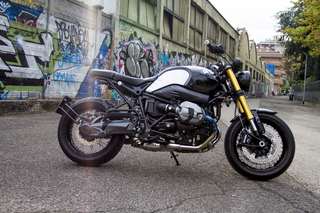 BMW R nineT — Fiancata destra in tre quarti posteriore, strada urbana sullo sfondo.