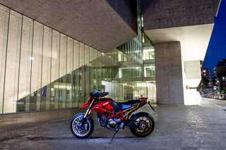 Ducati Hypermotard 1100 — Campo lungo notturno: la moto davanti a un edificio in vetro e cemento.