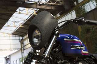 Harley-Davidson 883 Iron — Cupolino nero opaco e faro, lato sinistro, in un capannone con capriate.