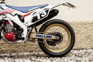 Honda CRF 450 E — Lato sinistro basso: forcellone Pro-Link, catena, corona, pedana, ruota oro.